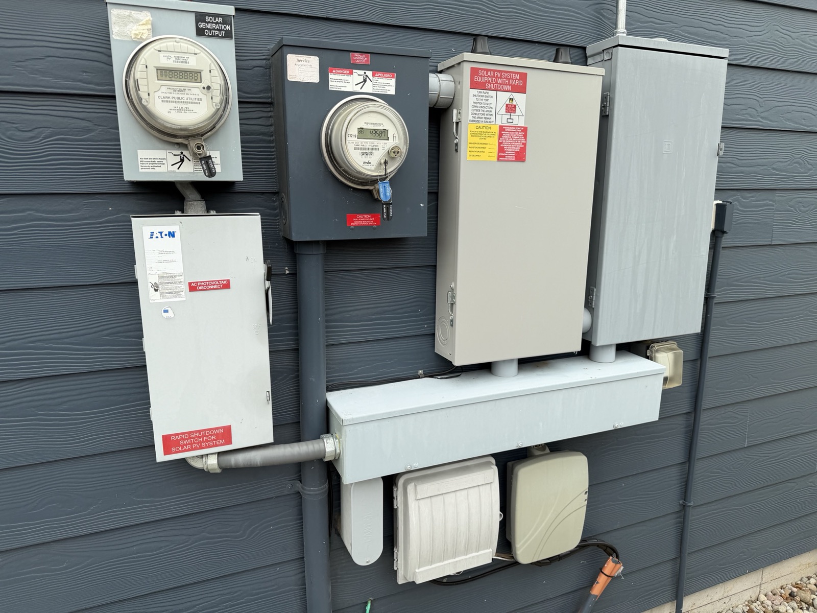 The exterior meter and disconnect cluster: the solar production meter and the Eaton safety switch below it, the generation net meter, the tan enclosure carrying the solar PV placards, and a grey Square D-marked enclosure.