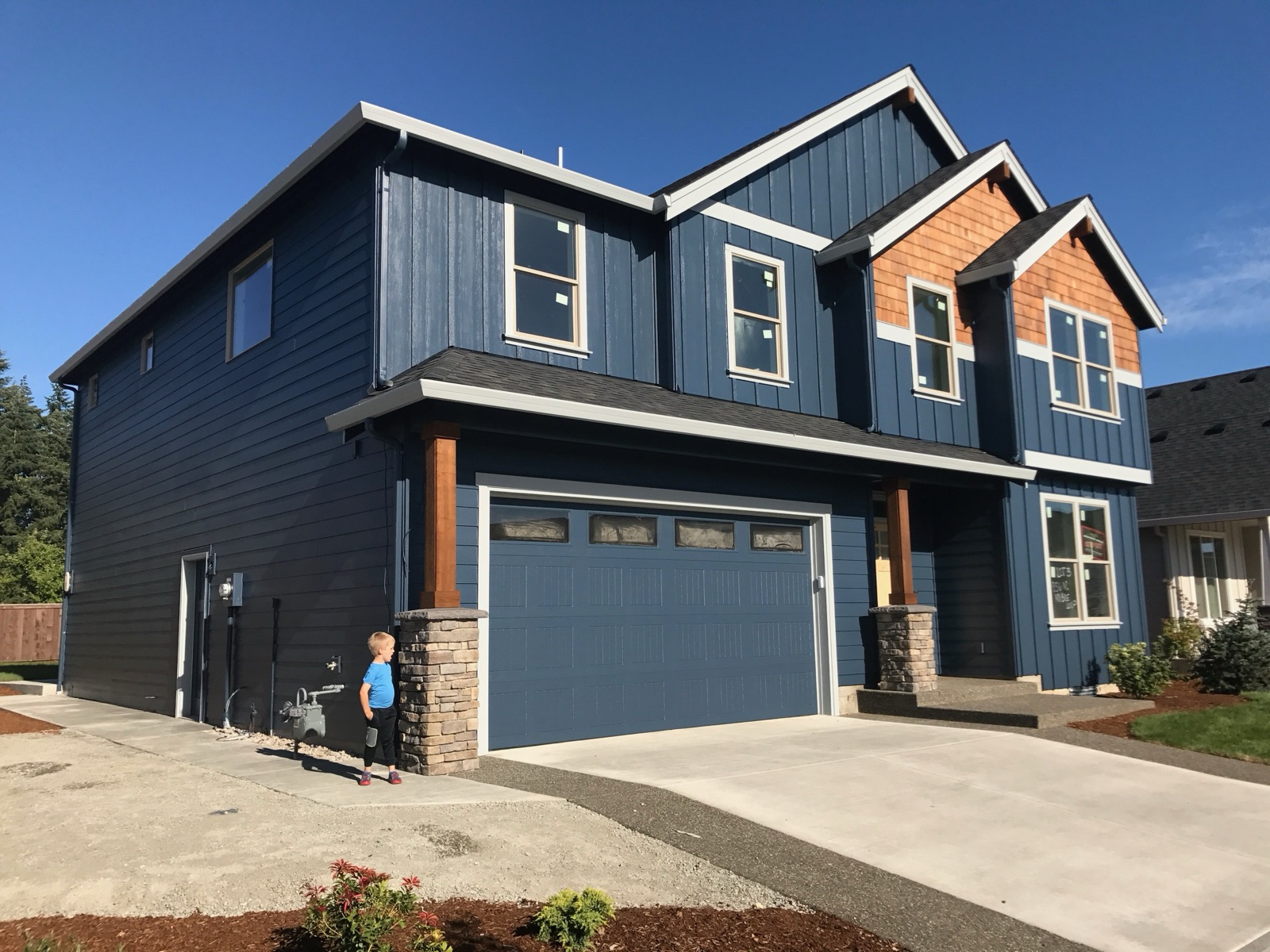 The finished home — deep-navy board-and-batten siding, cedar-shake gables, stacked-stone columns, on a corner lot.