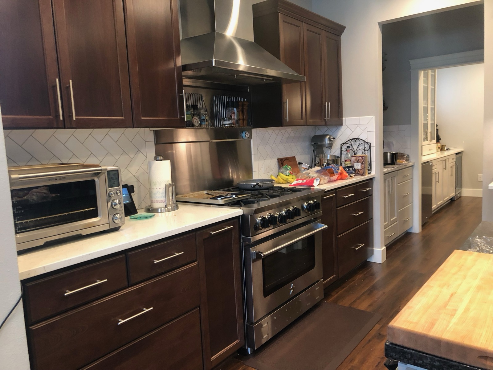 Stainless BlueStar professional range under a stainless chimney-style range hood, with dark wood cabinetry and herringbone tile backsplash.