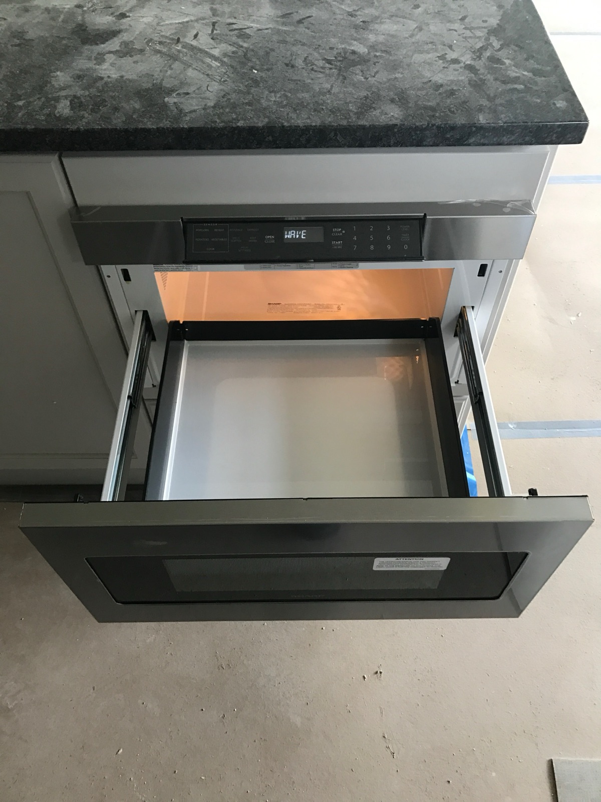 Open stainless microwave drawer set into island cabinetry, showing a Sharp interior nameplate and keypad.