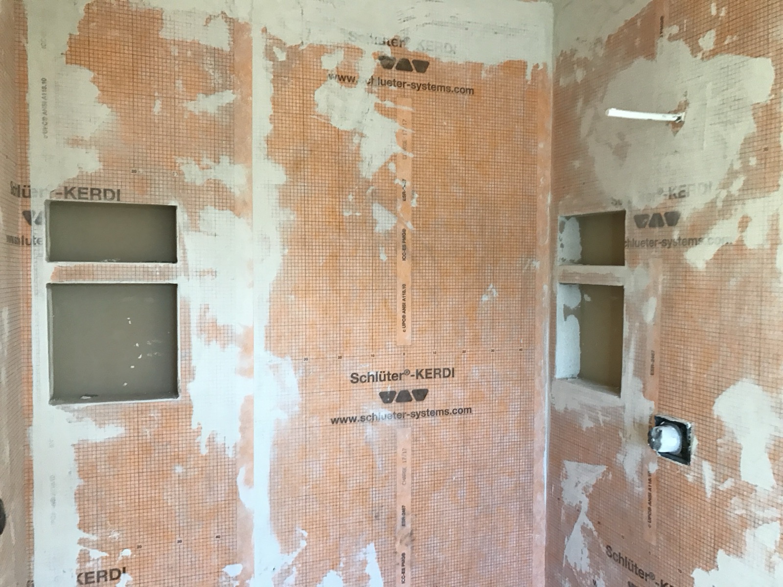 Pre-tile construction photo of the steam shower enclosure showing a fully membraned Schlüter-KERDI waterproofing system with banded seams across all three walls and three tiled niches.