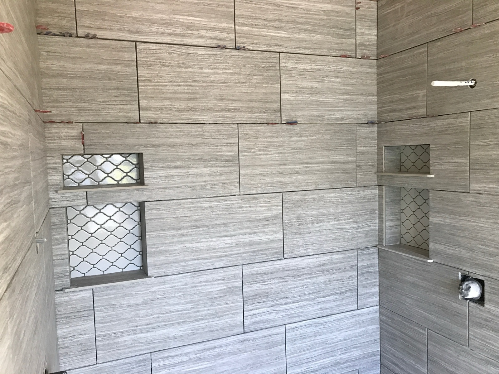Shower during construction, showing hand-set stone-look tile and two mosaic accent niches.
