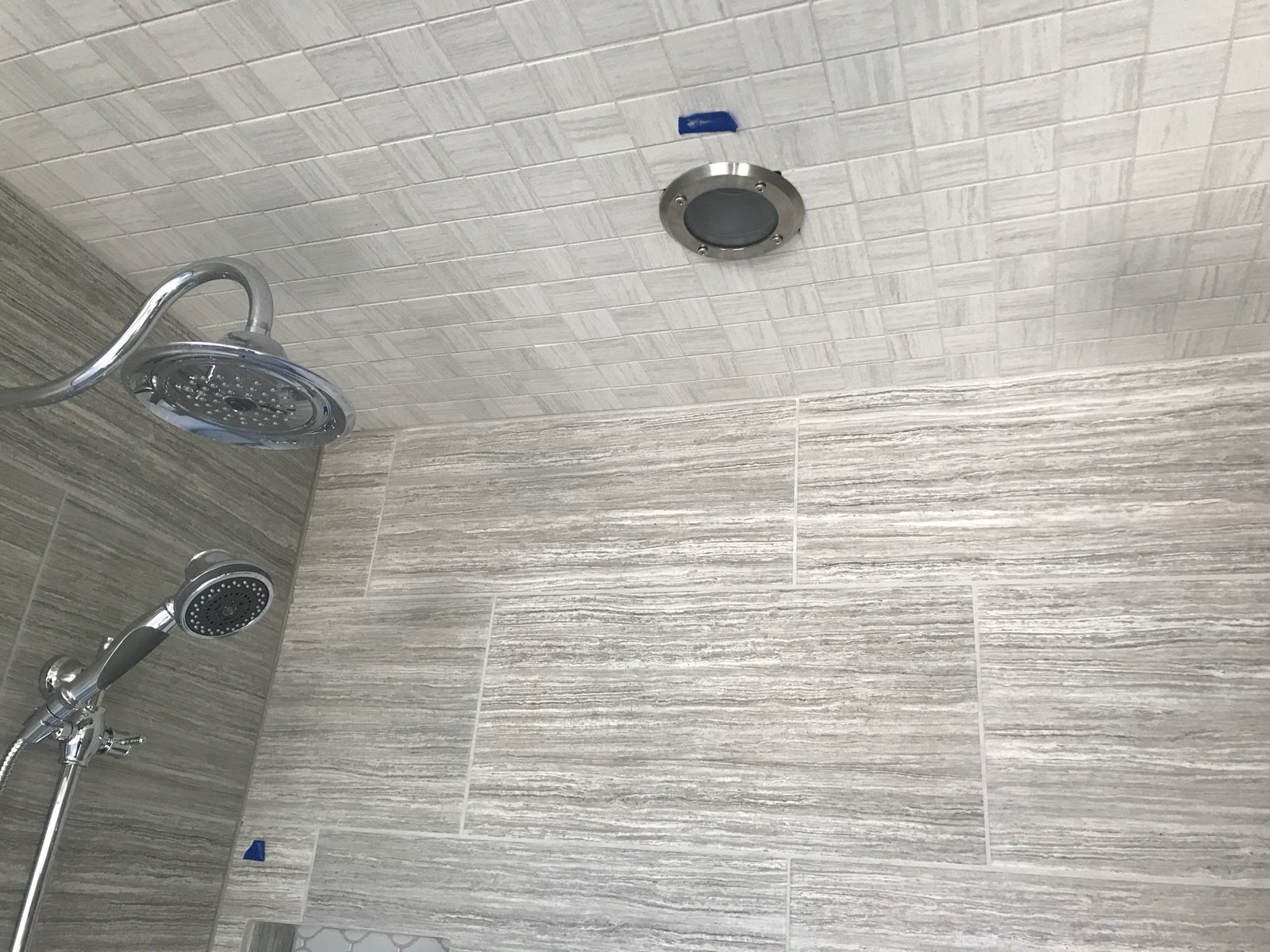 Tiled shower ceiling with the round steam-diffuser outlet next to the rain shower head.