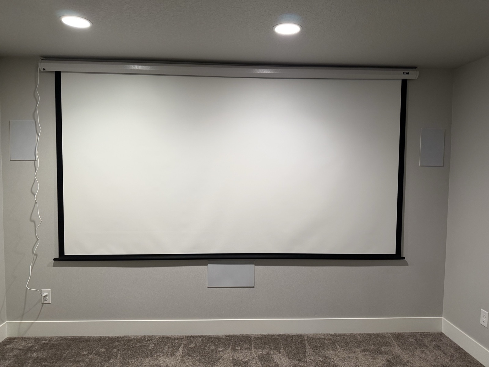 The motorized screen deployed, with in-wall speaker grilles to the left and right and one centered below the screen.