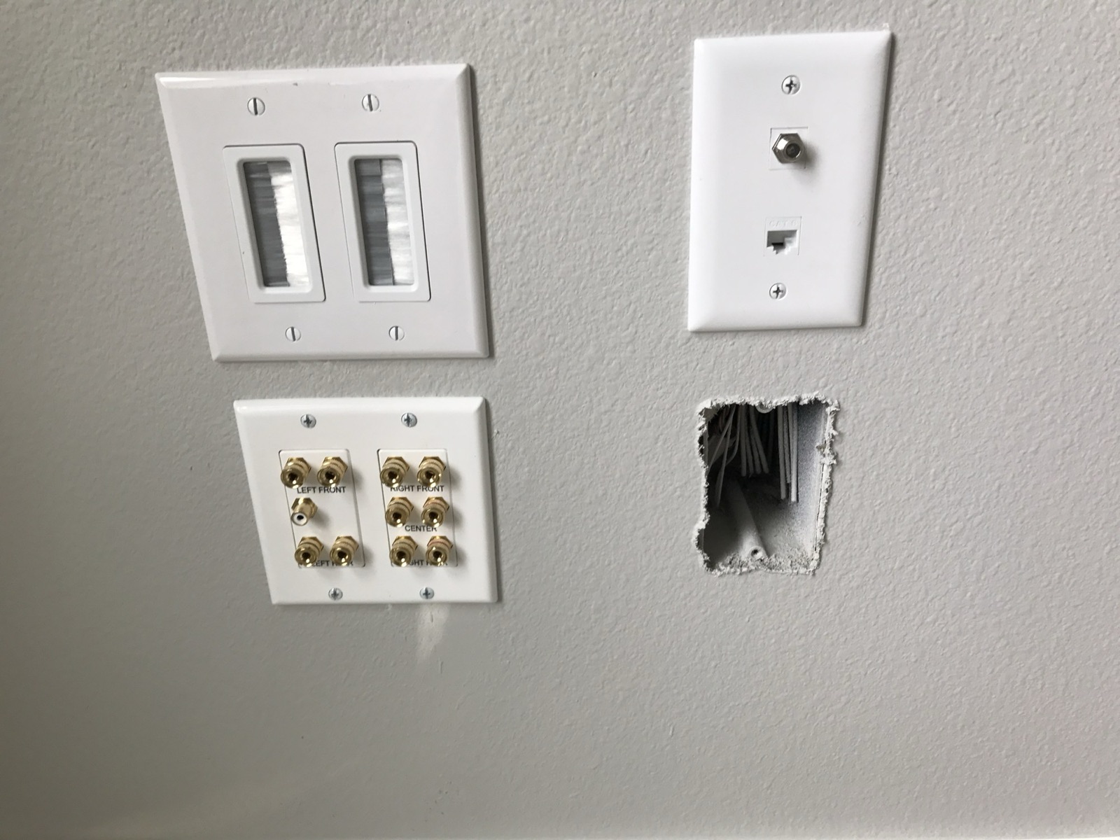 The same four wall plates photographed with nothing connected: a two-gang brush pass-through, a speaker binding-post plate whose channels are engraved LEFT FRONT, RIGHT FRONT, CENTER, LEFT REAR and RIGHT REAR with a white RCA subwoofer jack between them, a coax and Cat6 plate, and an open wall cut-out showing the cable bundle inside.