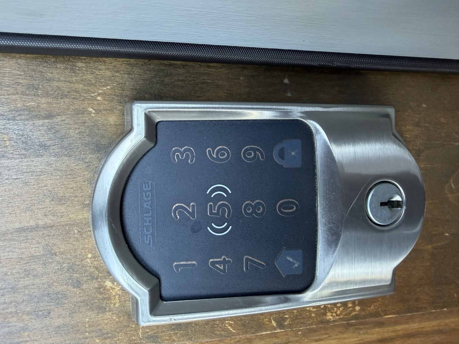 Schlage Encode touchscreen keypad deadbolt in satin nickel, mounted on an exterior door, showing the number pad and key cylinder.