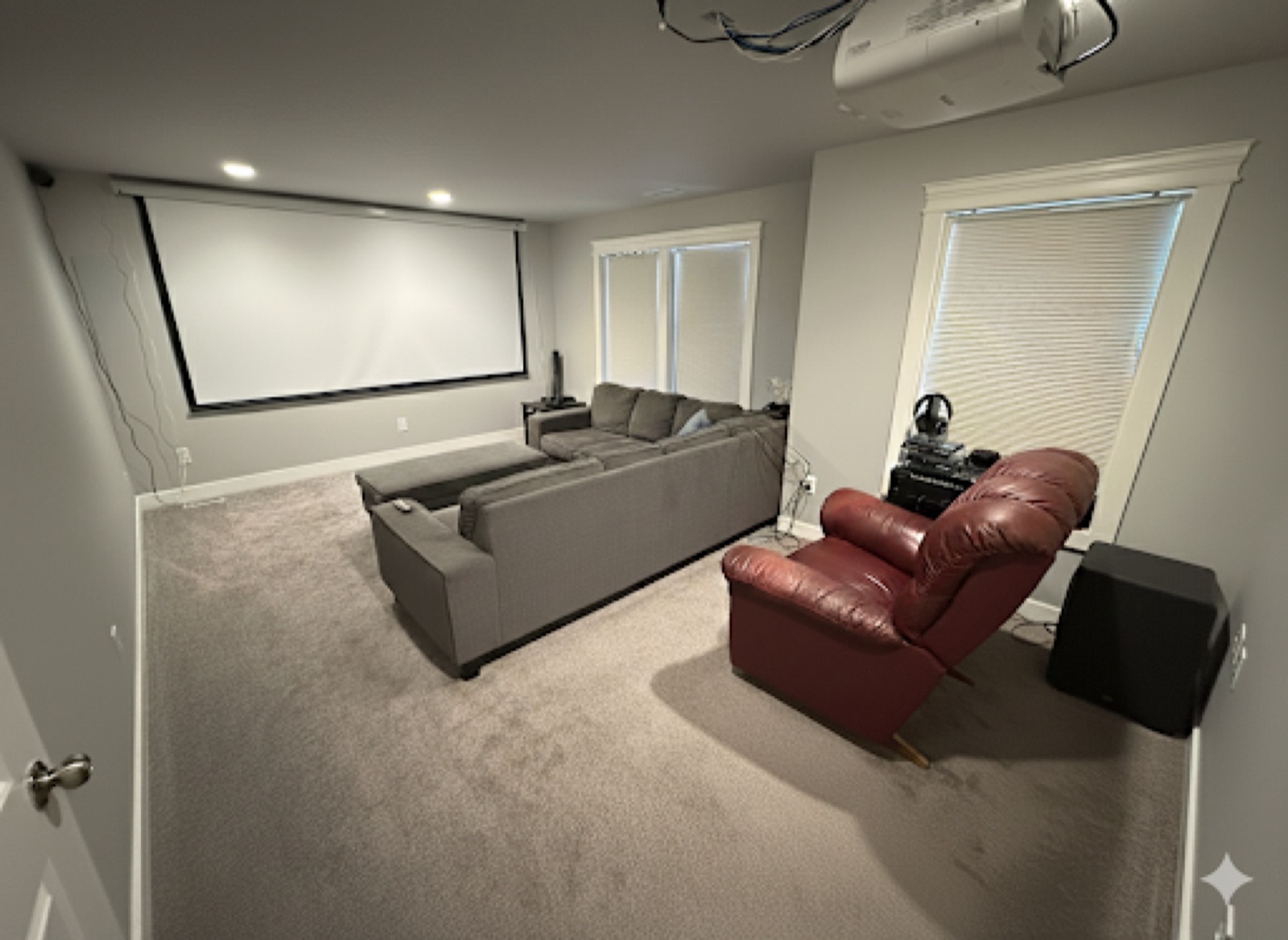Home theater with a large motorized projection screen, ceiling-mounted projector, sectional seating and a subwoofer.